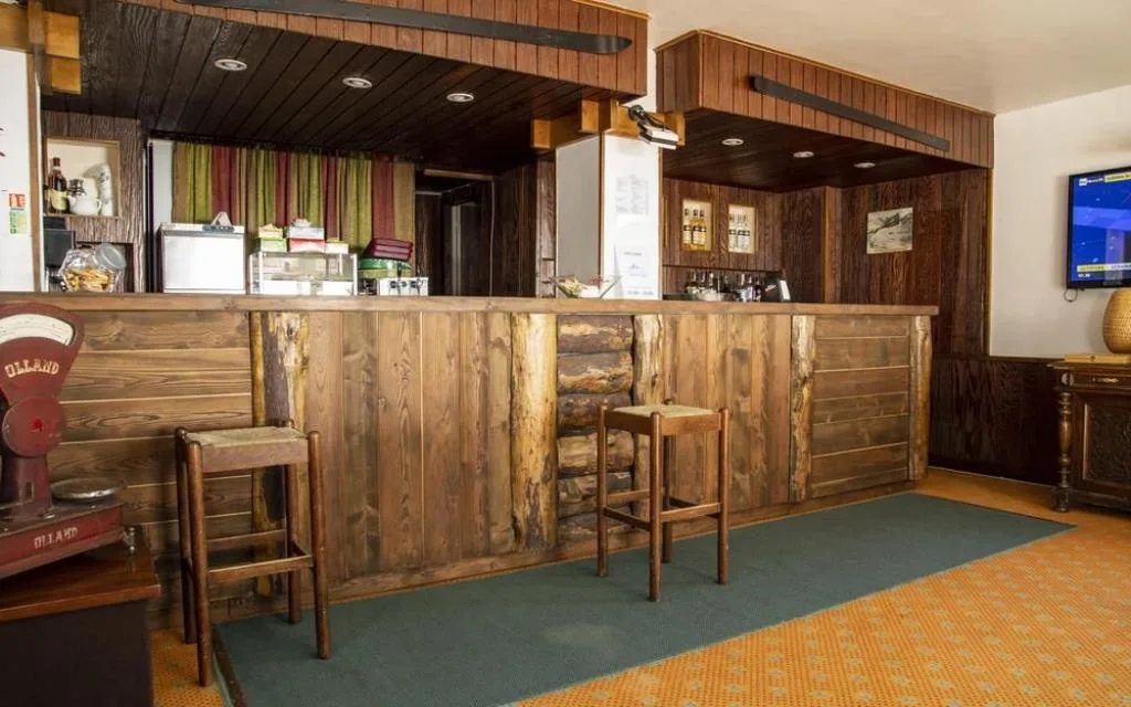 Bar interno con bancone in legno rustico, sgabelli e TV a parete