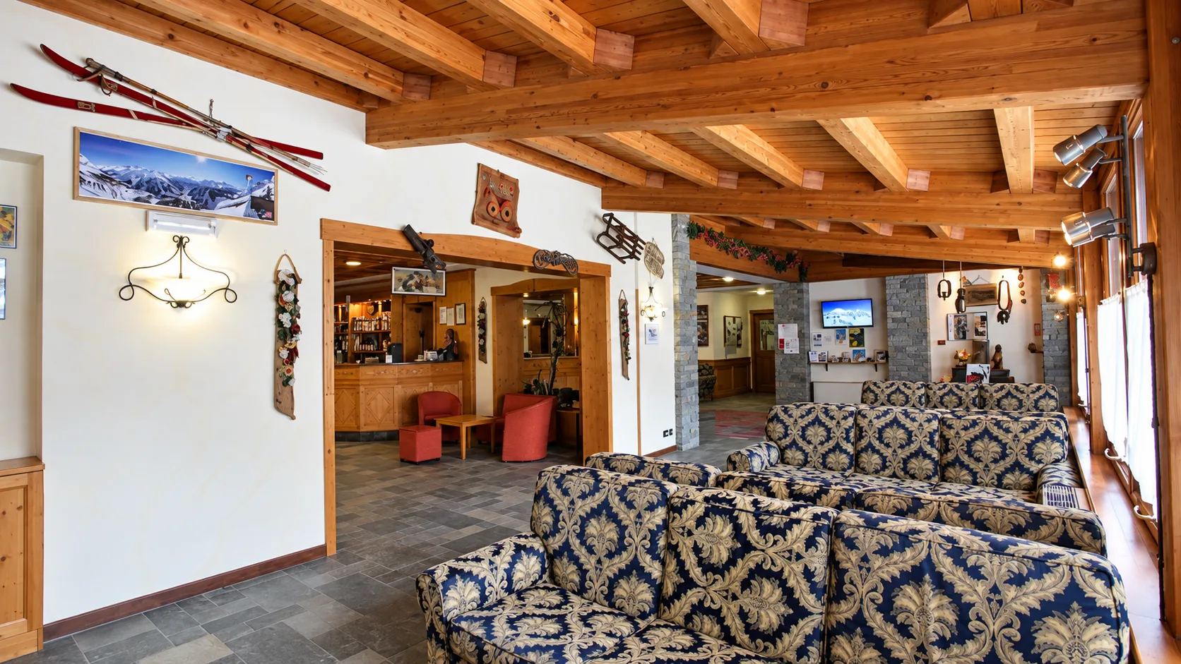 Area reception e lounge con divani decorati, soffitto in travi di legno e decorazioni a tema sci