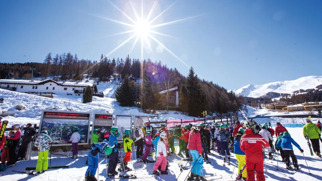 Sciatori in abbigliamento colorato riuniti ai piedi delle piste sotto il sole