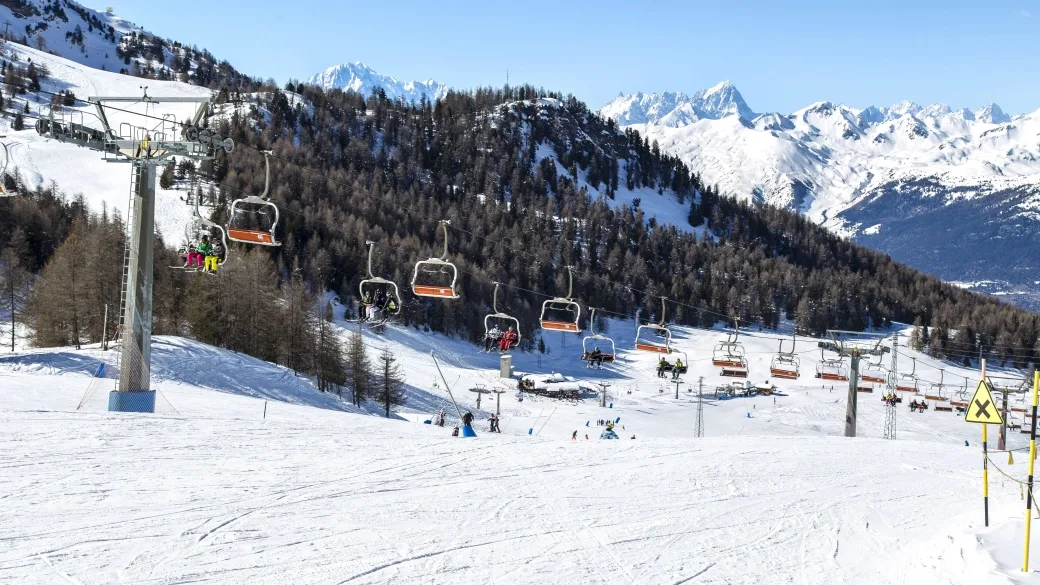 Seggiovia e piste da sci con panorama di montagne innevate e boschi