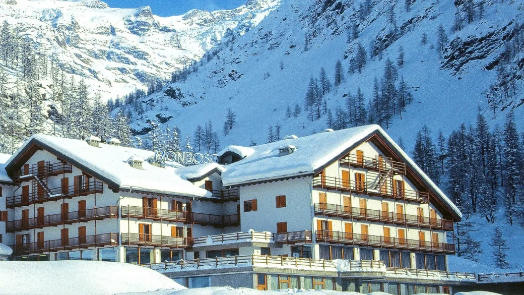Facciata dell'hotel con tetti innevati e insegna Monboso tra le montagne imbiancate