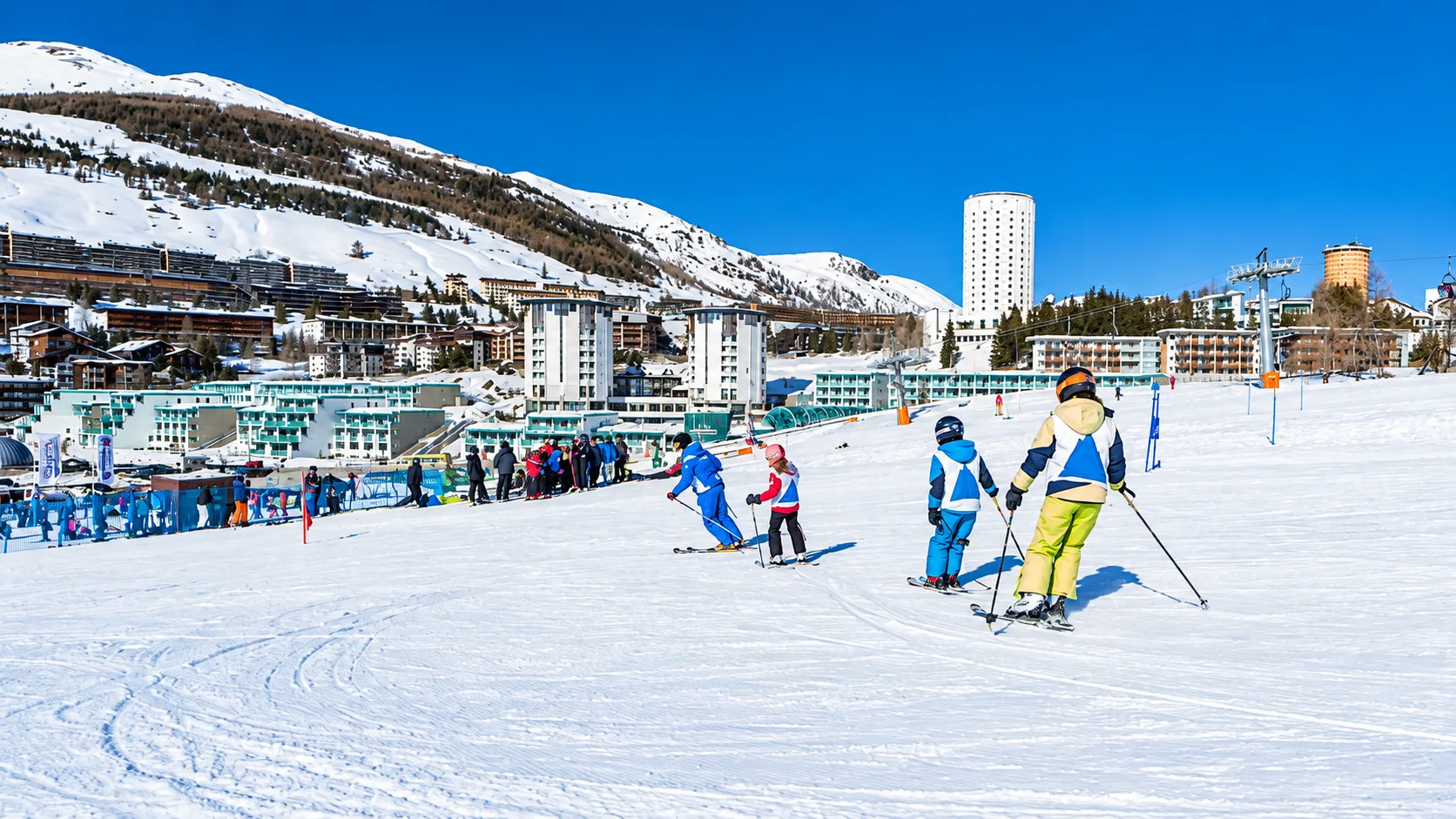 Sciatori e bambini sulle piste da sci con l'hotel e la località montana sullo sfondo