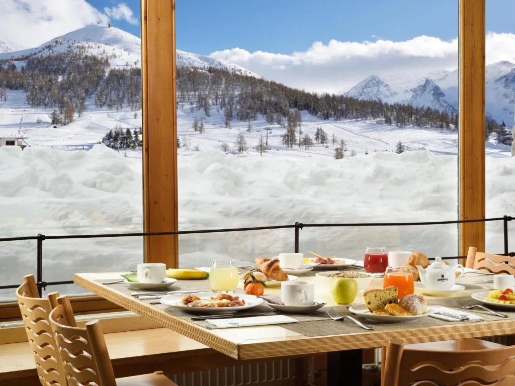 Tavolo della colazione con cibo e bevande davanti a vetrata con vista sulle montagne innevate