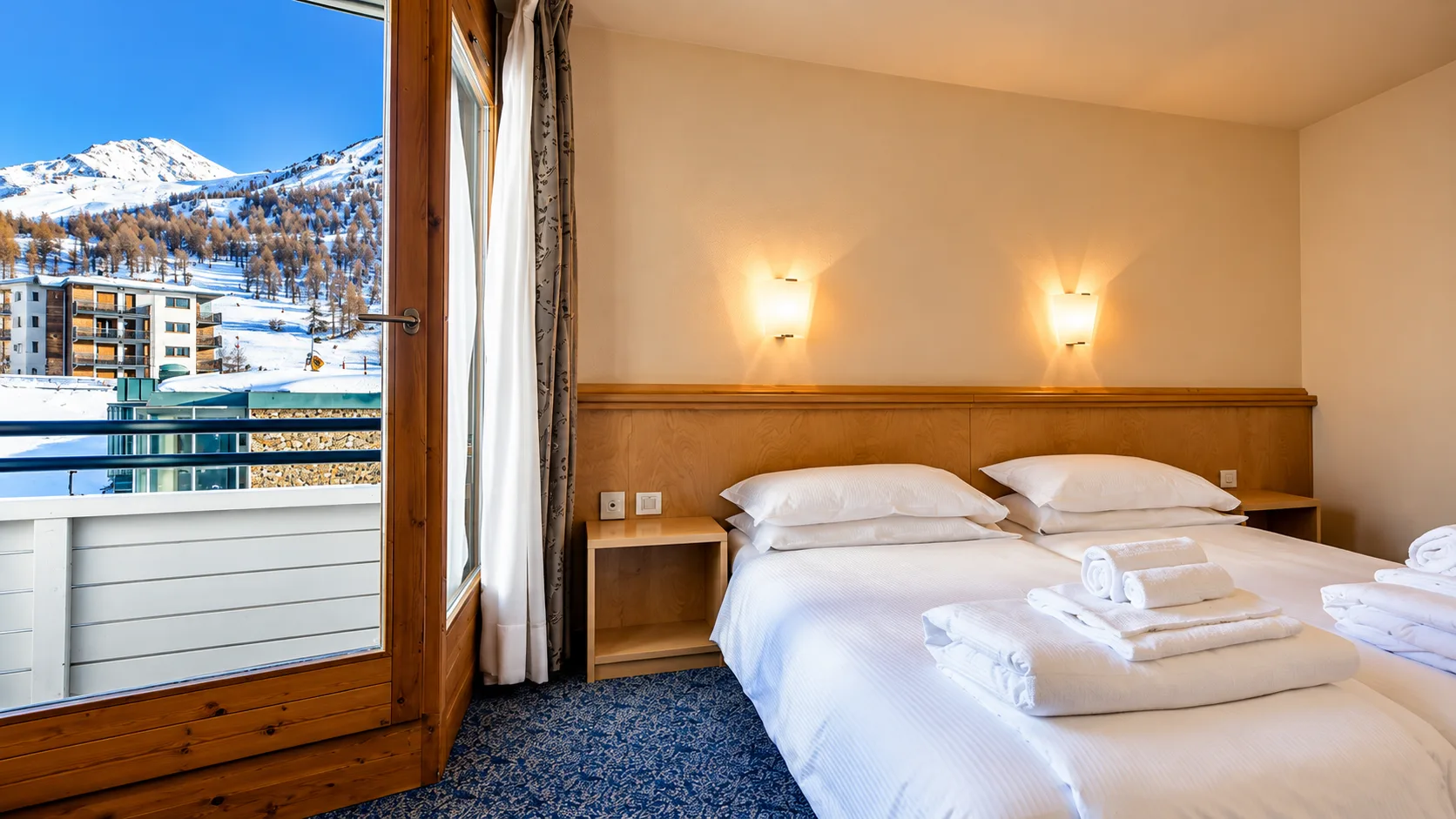 Camera con letto matrimoniale, asciugamani e balcone con vista sulle montagne innevate