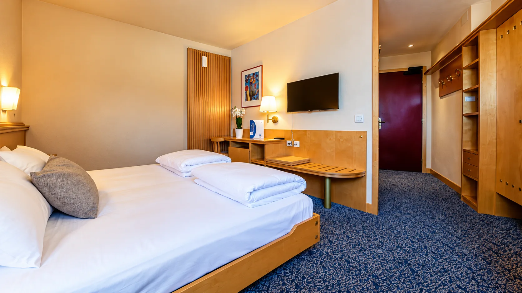 Camera doppia con letto, scrivania, TV e pavimento in moquette blu