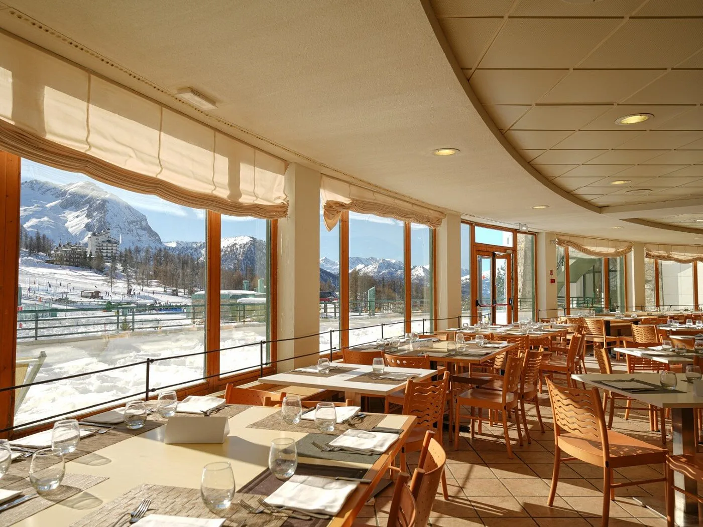 Sala ristorante luminosa con tavoli apparecchiati e ampie finestre sul paesaggio montano