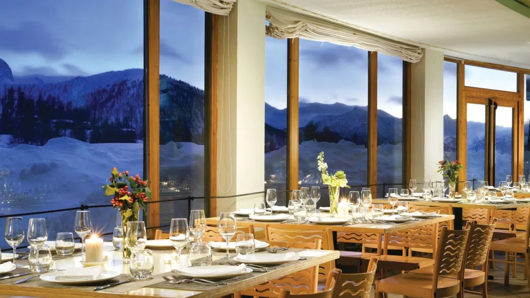 Ristorante con tavoli apparecchiati e grandi vetrate panoramiche sulle montagne al crepuscolo