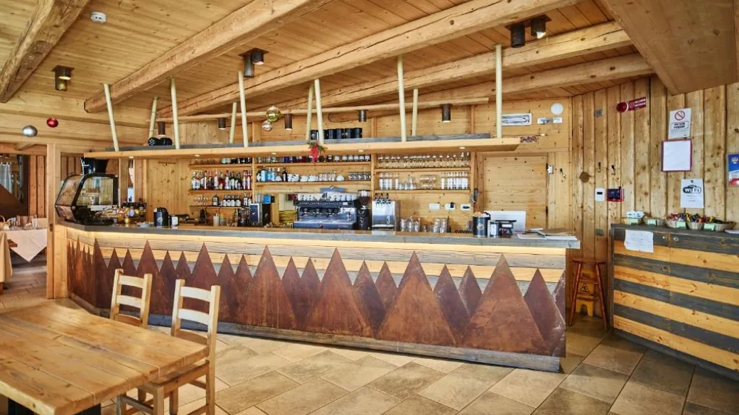 Bancone bar in legno con decorazione a montagne e scaffali con bicchieri e bottiglie