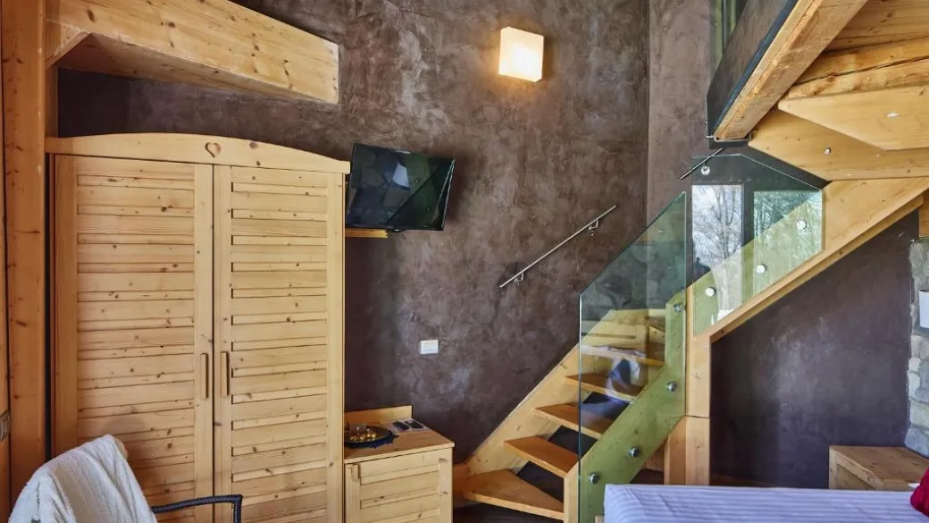 Camera su due livelli con scala in legno e vetro, armadio e TV a parete