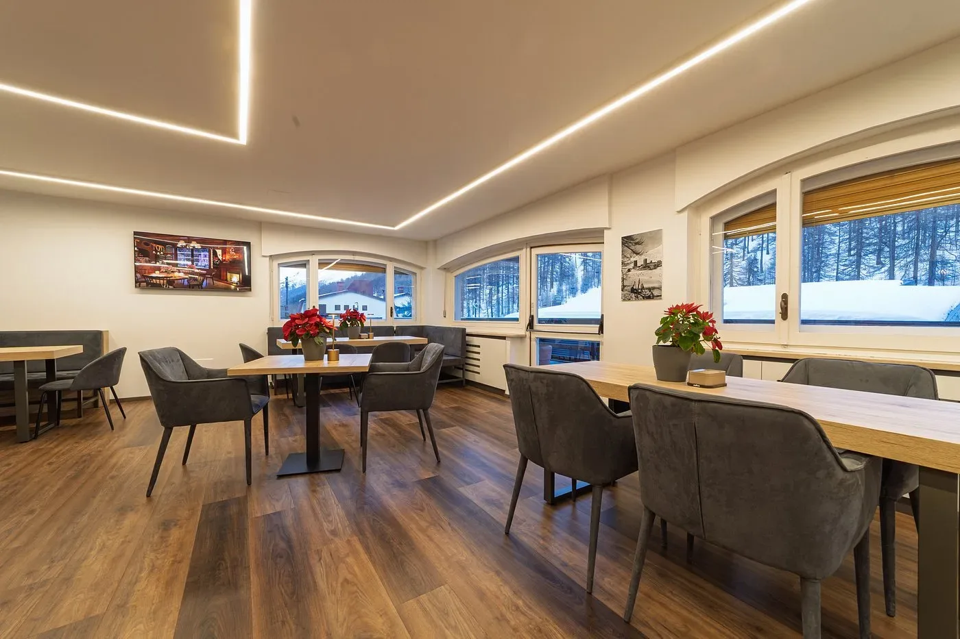 Sala interna luminosa con tavoli in legno, poltrone grigie e vista sulla neve