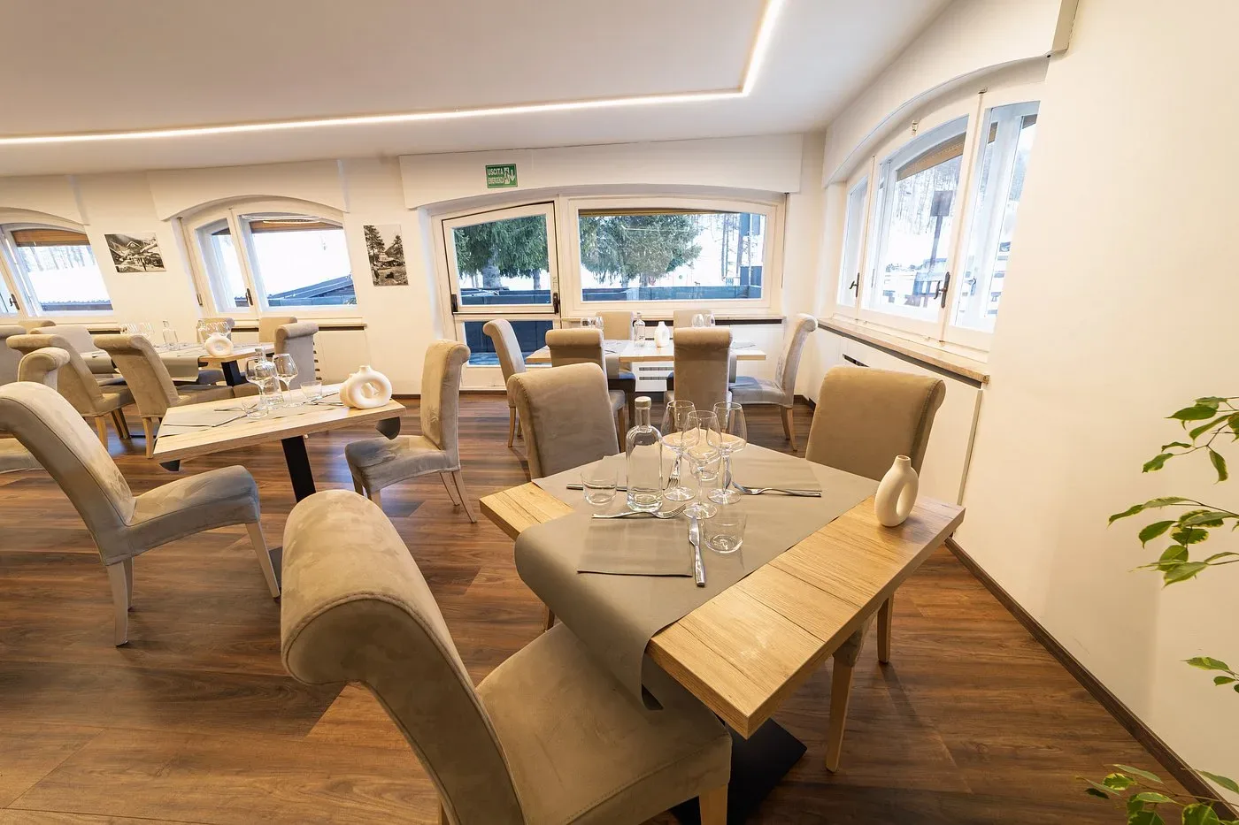 Ristorante luminoso con tavoli, sedie beige e vista sugli abeti innevati