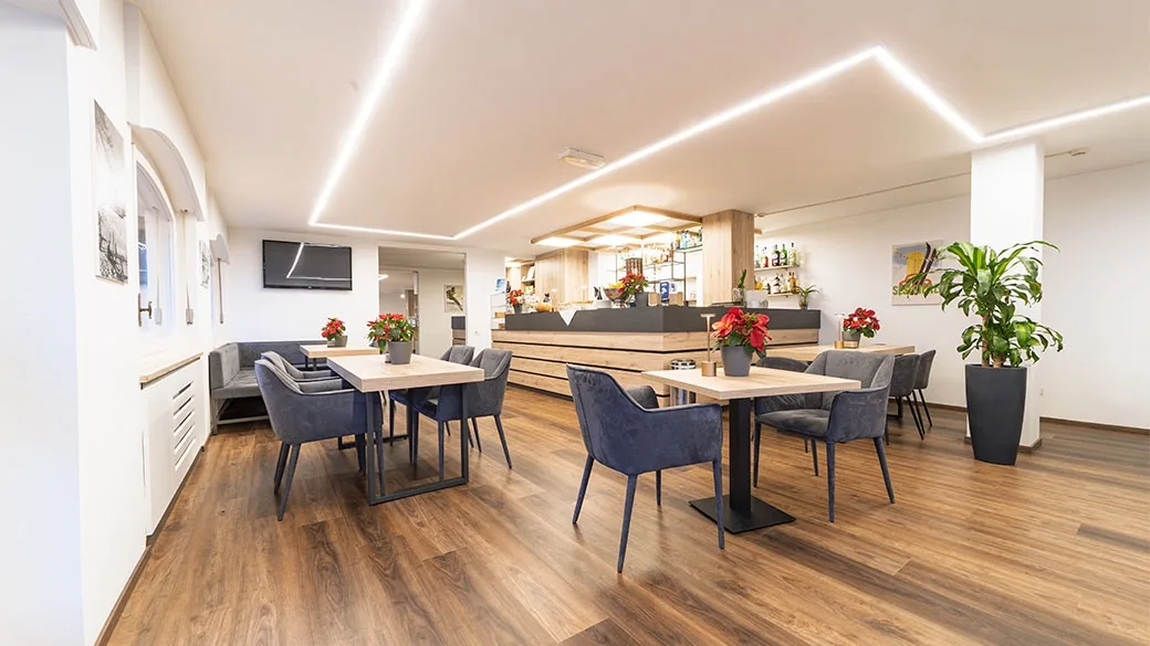 Ampia sala comune con tavoli, sedute e bancone bar in legno moderno