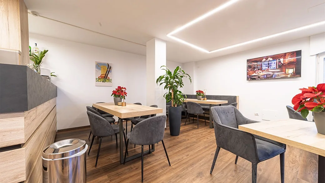 Area ristoro con tavoli in legno, sedie grigie e piante decorative