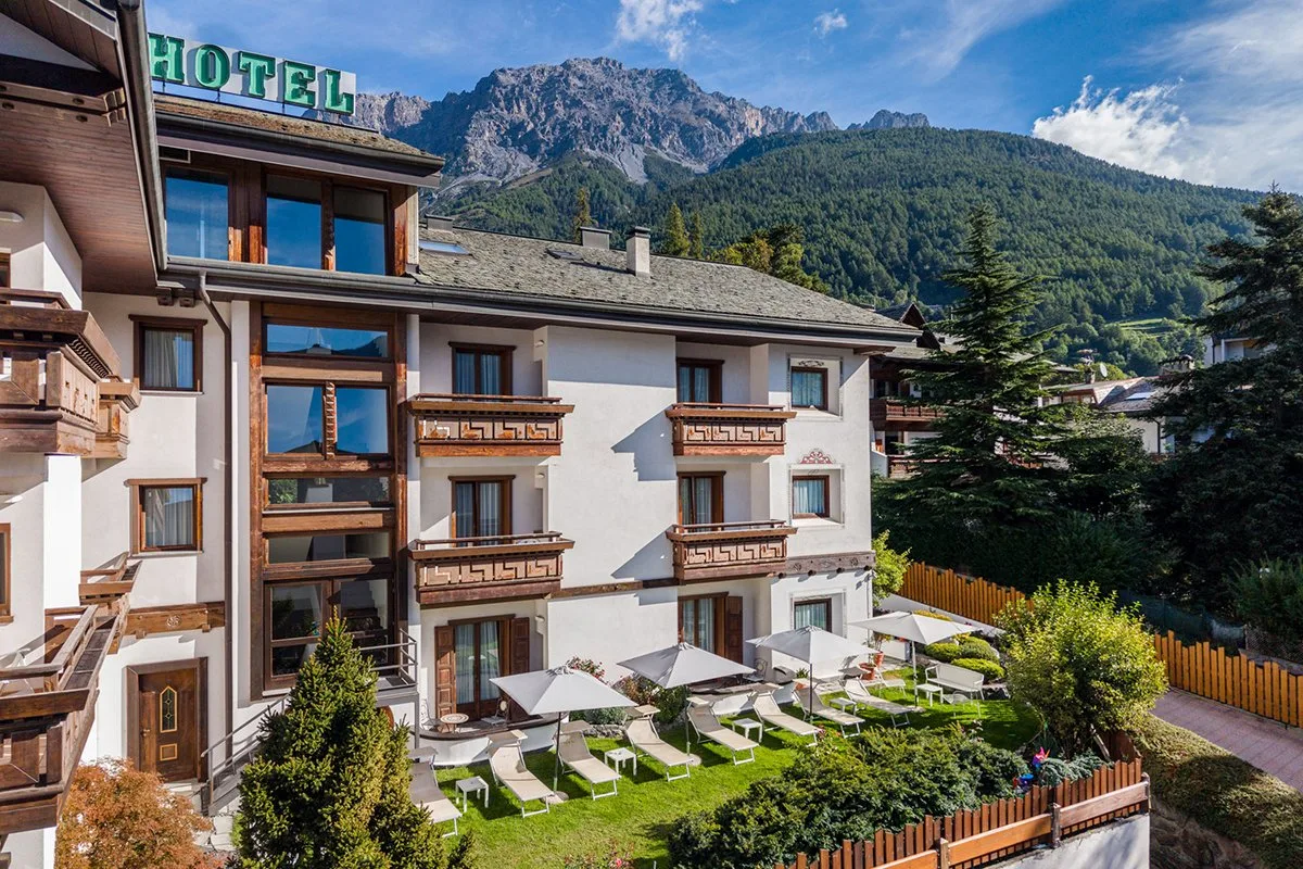 Giardino dell'hotel con lettini, ombrelloni e vista sulle montagne in estate