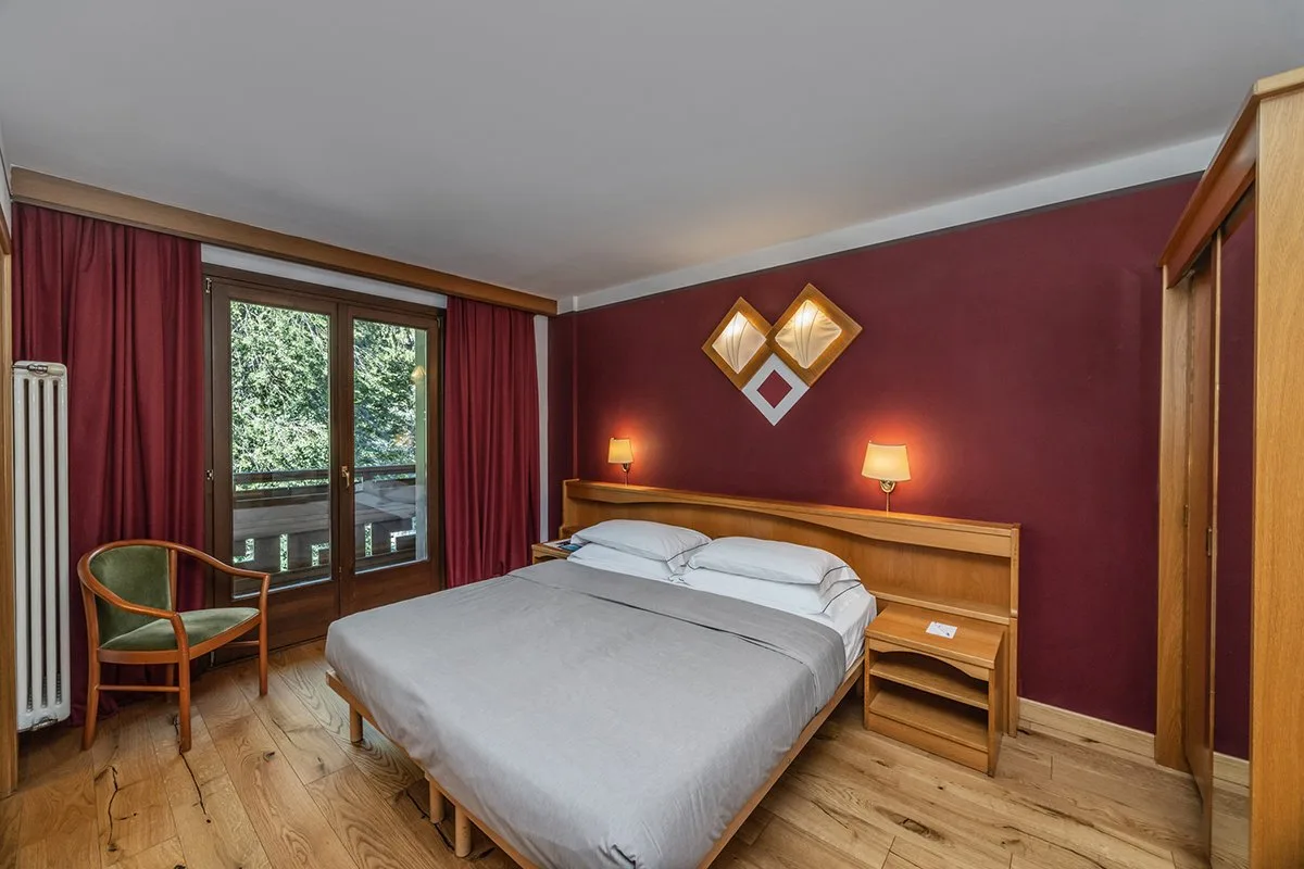 Camera matrimoniale con parete bordeaux, letto e accesso al balcone