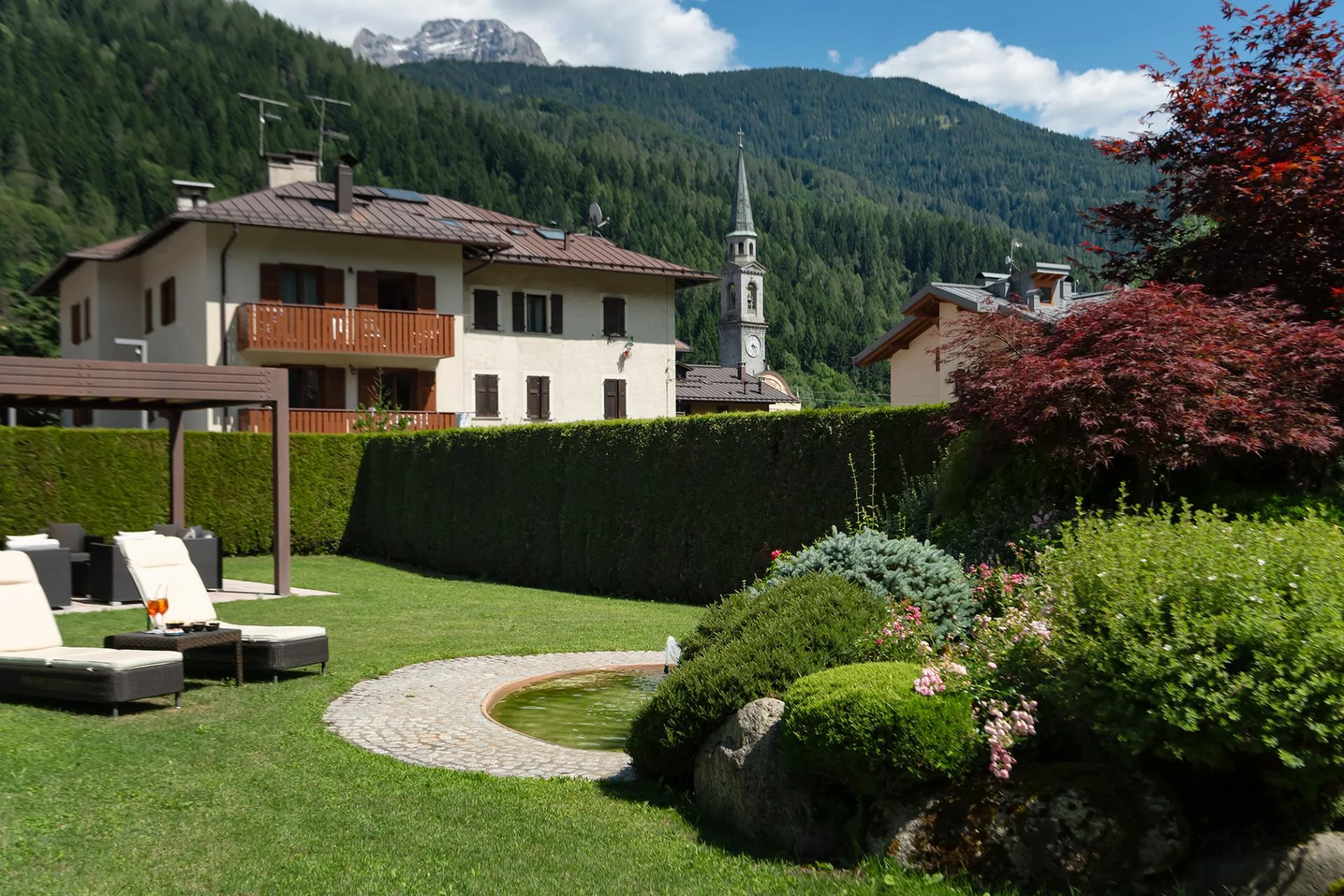 Giardino curato con laghetto e vista su montagne boscose e campanile