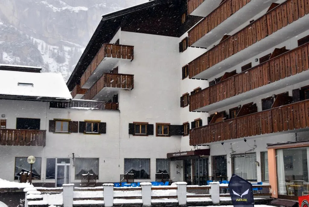 Facciata dell'hotel con balconi in legno durante una nevicata, tavoli e sedie esterni coperti di neve