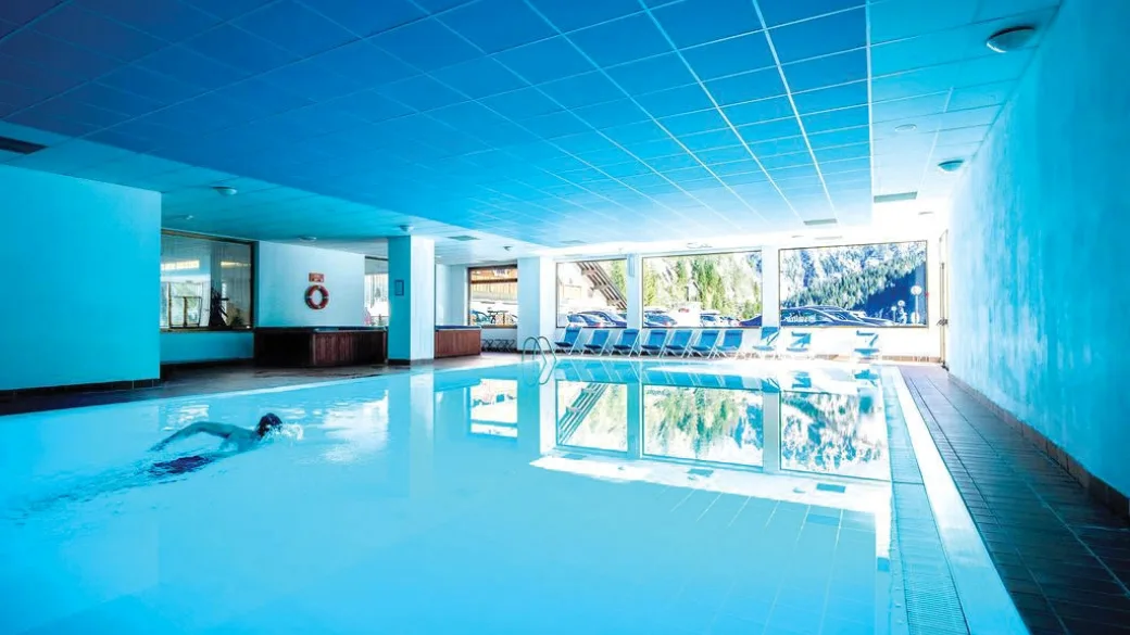 Piscina interna con lettini e grandi finestre sulla natura, nuotatore in acqua