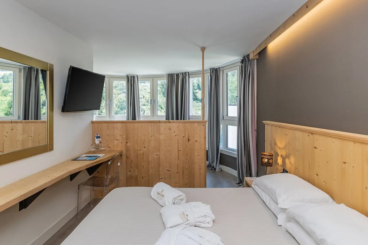 Camera con letto, scrivania, TV e ampie finestre affacciate sul bosco