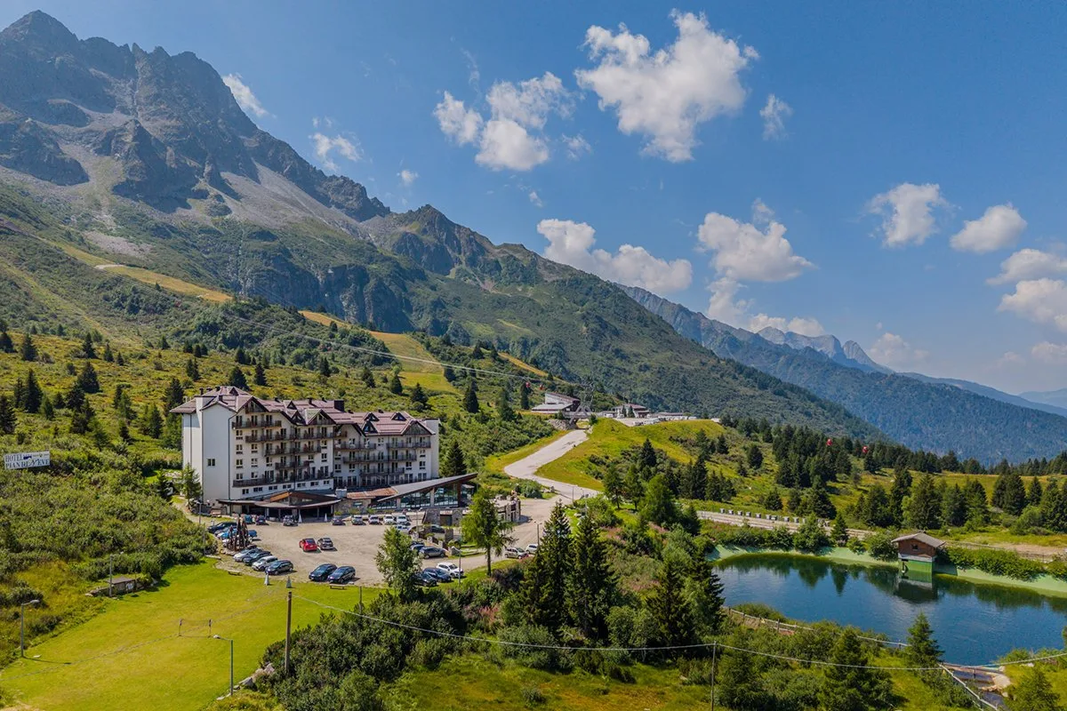 Veduta aerea estiva dell'hotel con laghetto, prati e montagne sullo sfondo