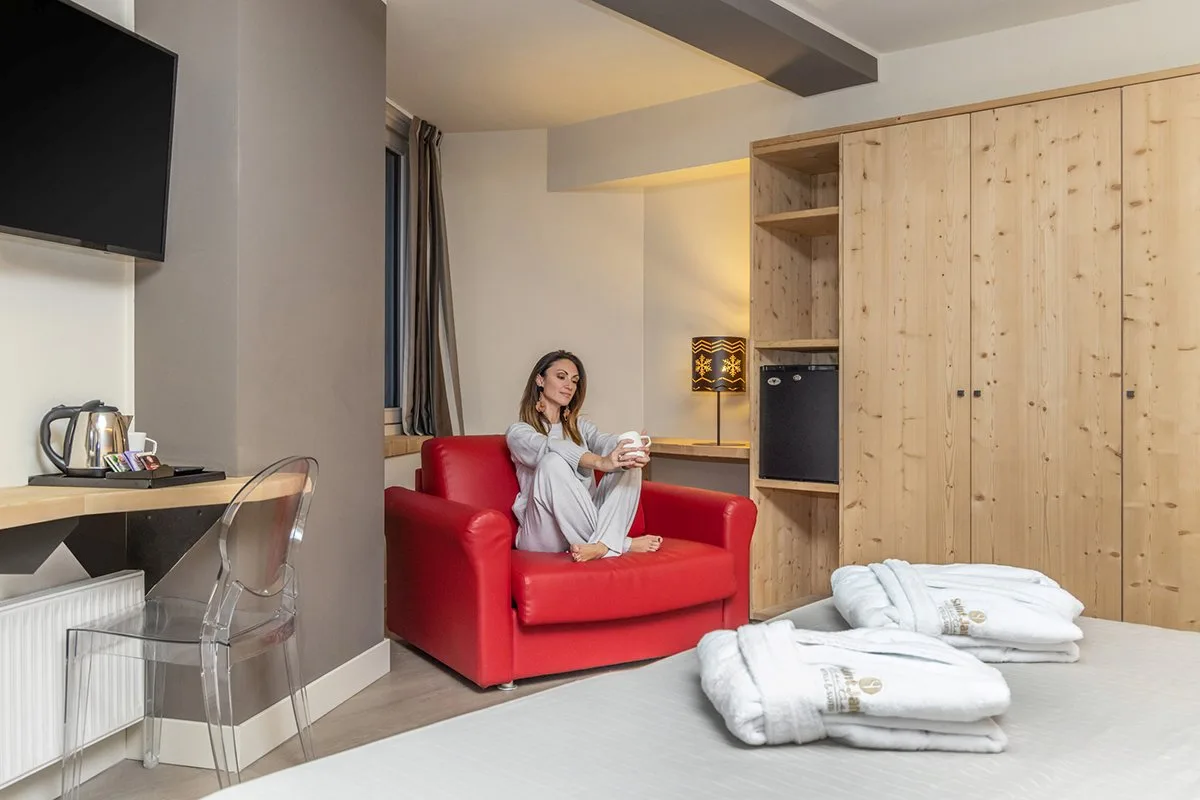 Camera confortevole con poltrona rossa, armadio in legno e accappatoi sul letto