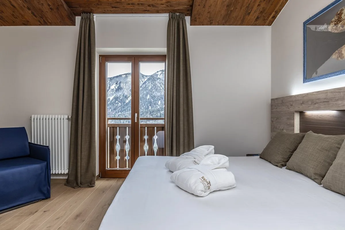 Camera moderna con letto matrimoniale, divanetto blu e balcone vista montagne