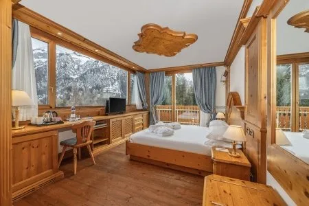 Camera in legno con letto matrimoniale, scrivania e grandi vetrate sul paesaggio innevato