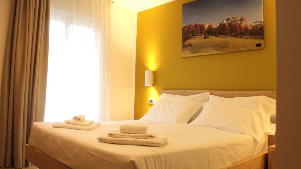 Camera matrimoniale con parete gialla, letto in legno e quadro delle Dolomiti
