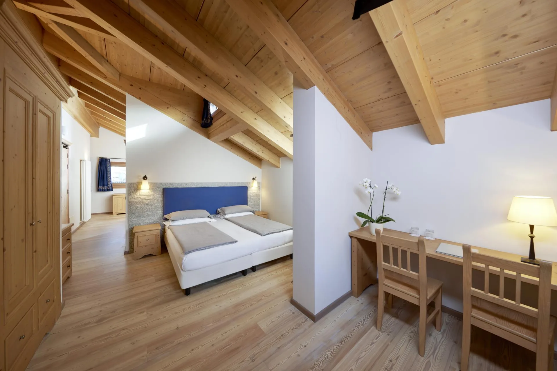 Camera mansardata con travi in legno a vista, letto e scrivania