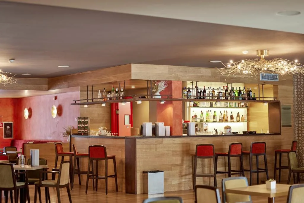 Bar dell'hotel con bancone in legno, sgabelli e ampia selezione di bottiglie