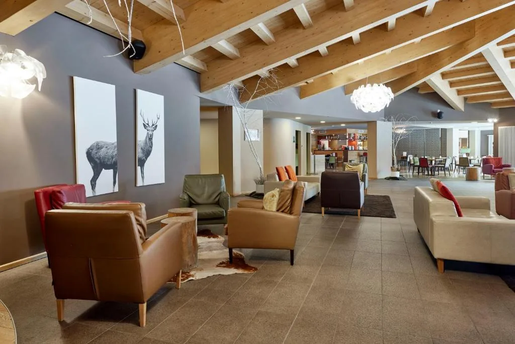 Lounge dell'hotel con poltrone in pelle, quadri di cervi e soffitto in travi di legno