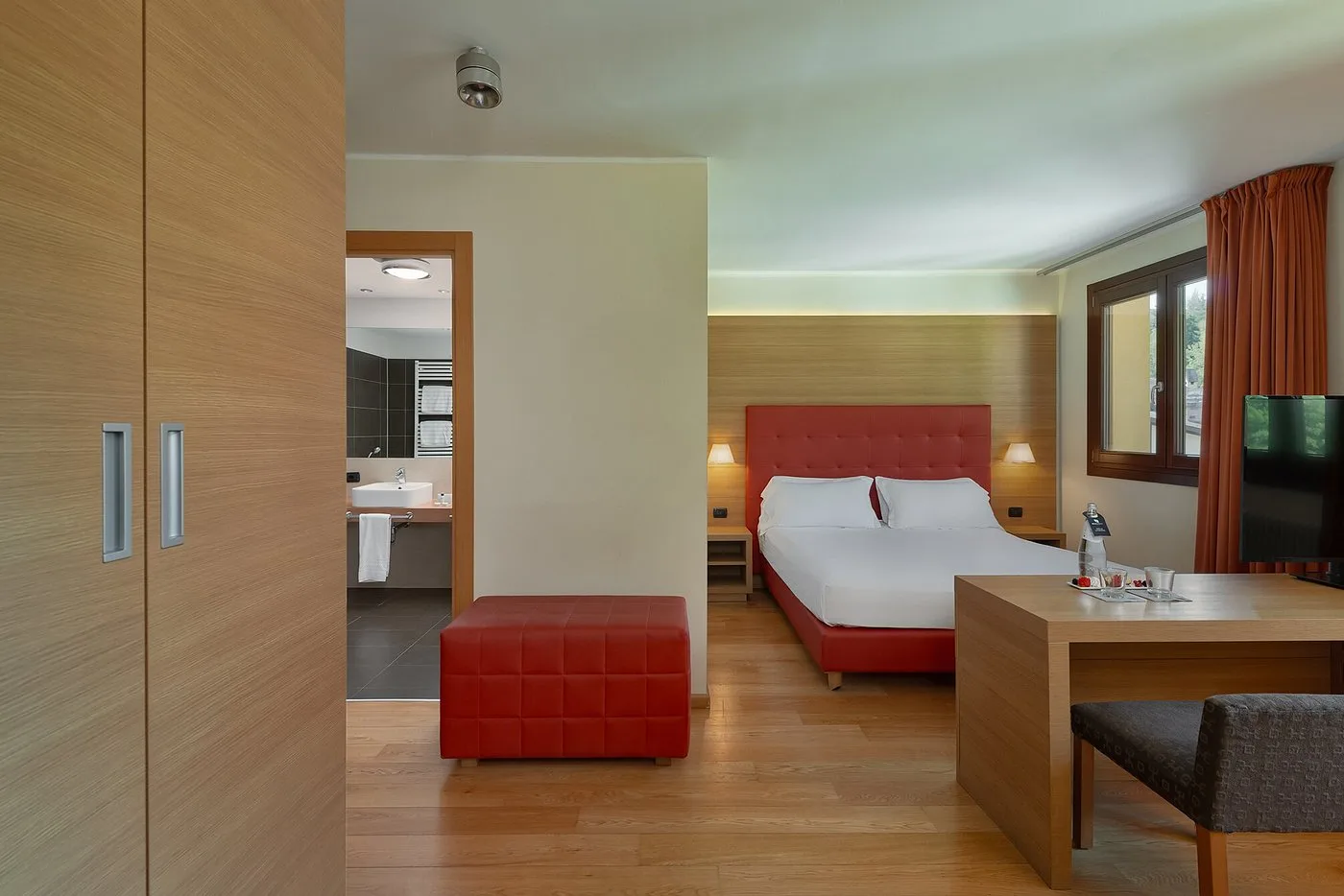 Camera con letto matrimoniale, testiera rossa, pouf e accesso al bagno