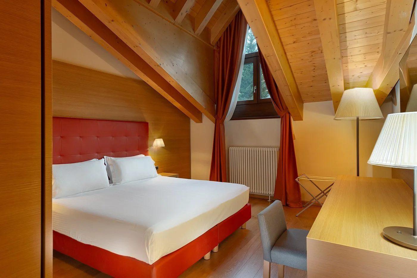 Camera mansardata con travi di legno a vista, letto matrimoniale e scrivania