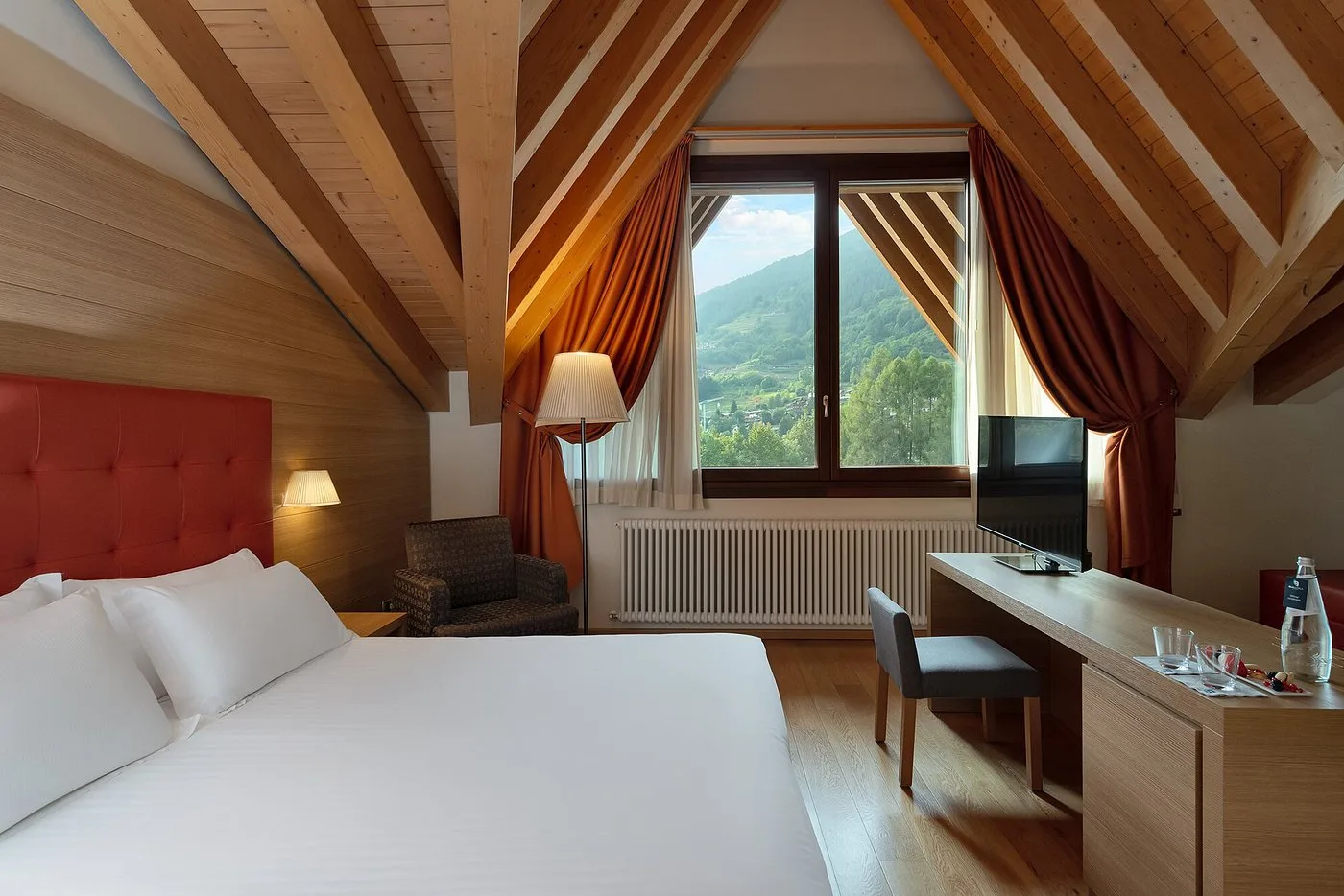 Camera mansardata con travi in legno, scrivania e finestra con vista sulla valle