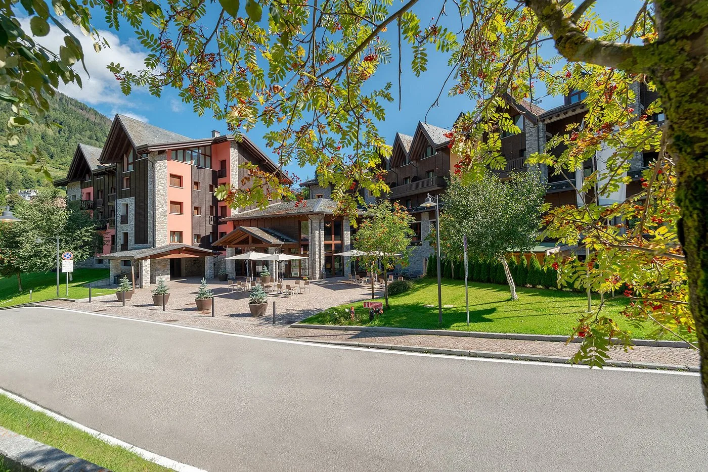 Esterno estivo dell'hotel con ingresso, giardino fiorito e alberi da frutto