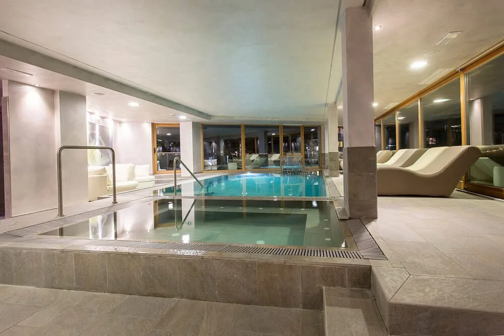 Piscina interna illuminata della spa con lettini relax e ampie vetrate serali