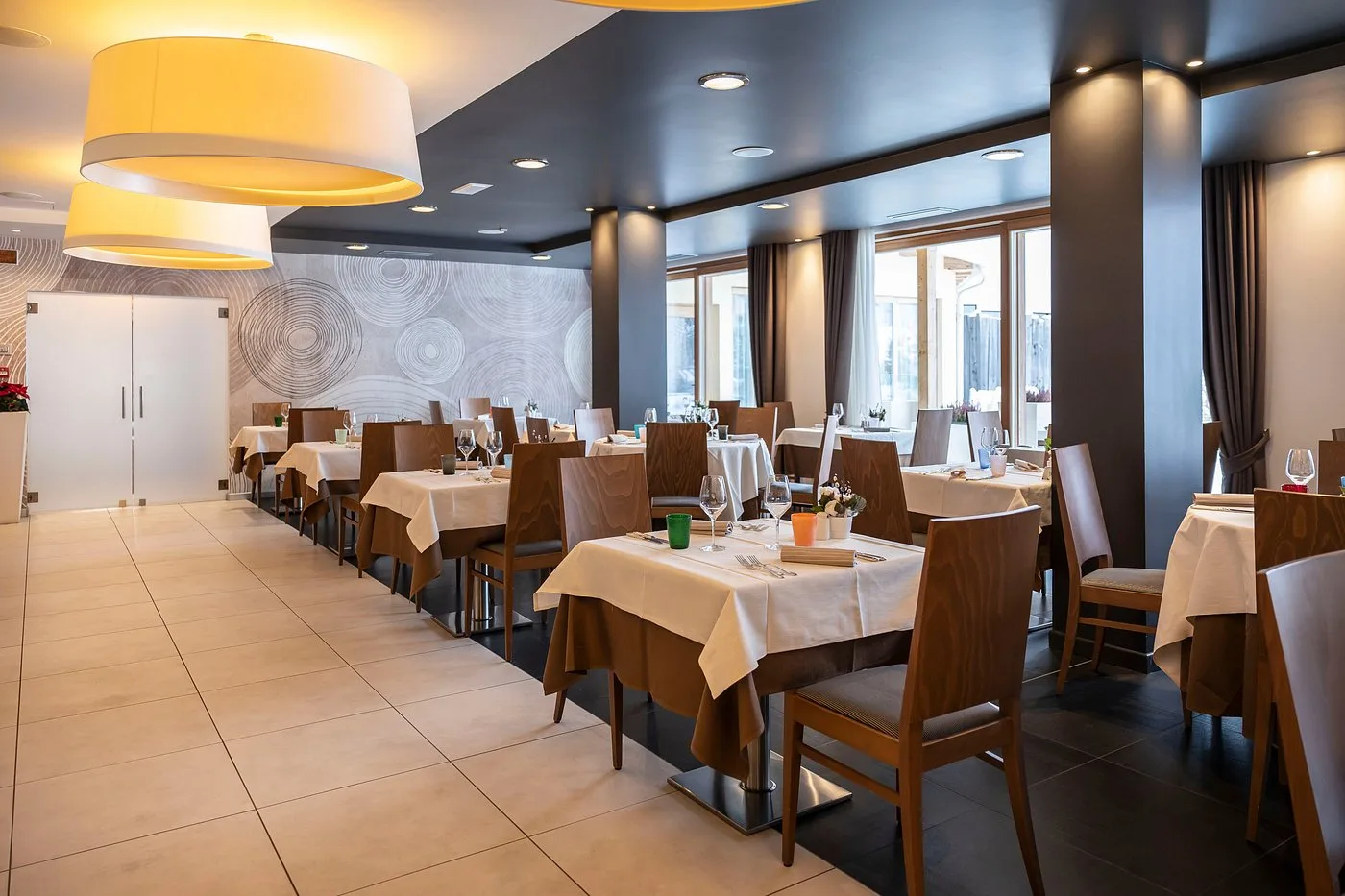 Sala ristorante elegante con tavoli apparecchiati, lampade gialle e parete decorata