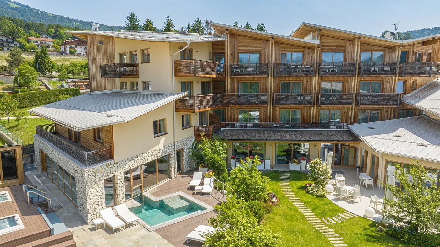 Vista aerea estiva dell'hotel con giardino verde, piscina esterna e facciata in legno e pietra