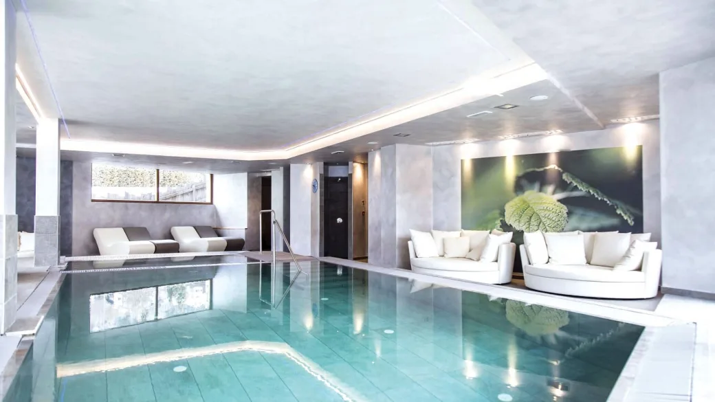 Piscina coperta dell'hotel con acqua turchese, lettini e divani bianchi