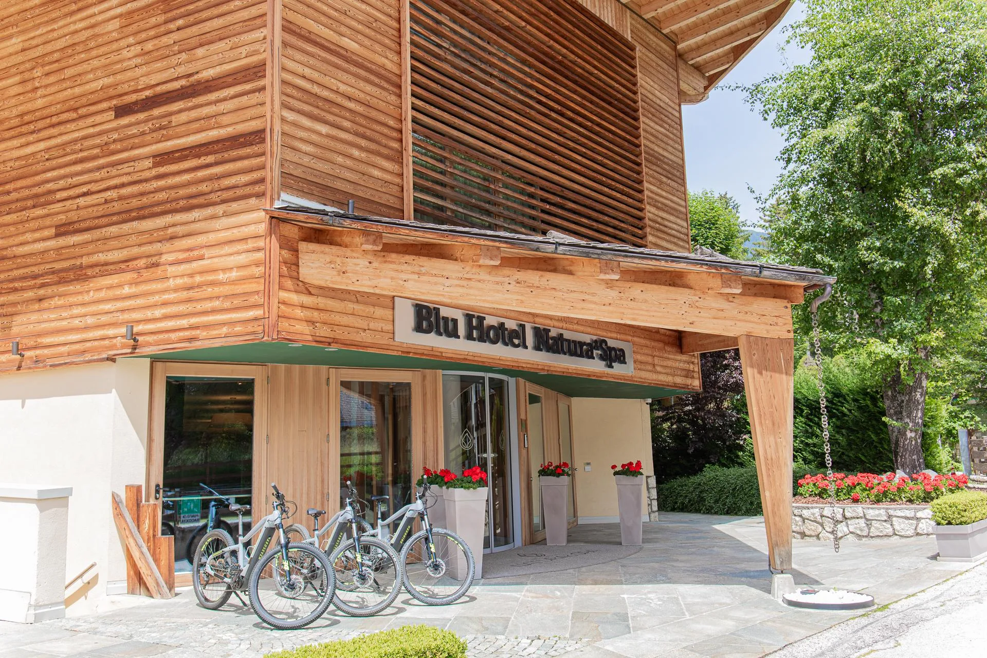 Ingresso del Blu Hotel Natura & Spa con facciata in legno e biciclette parcheggiate