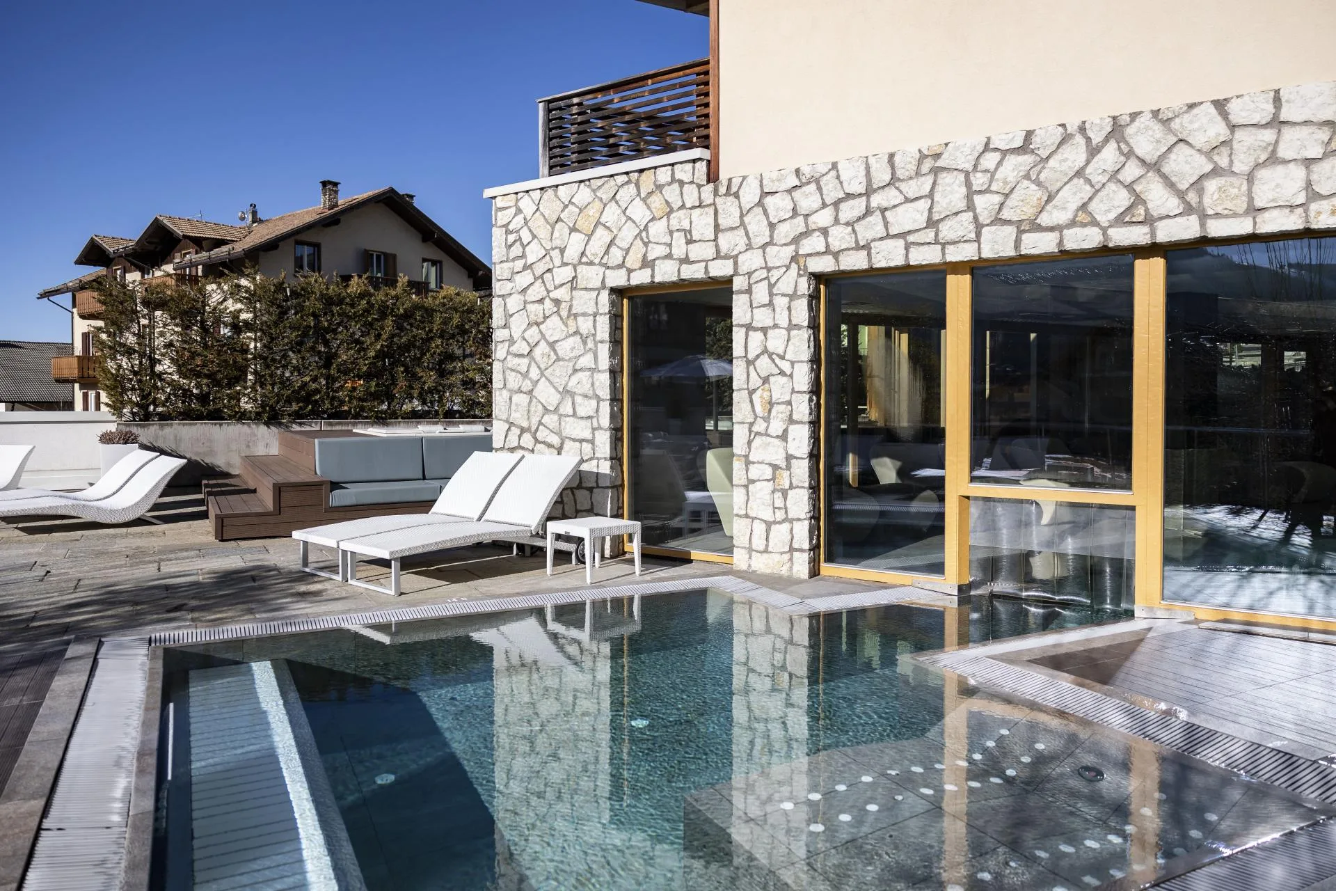 Piscina esterna con acqua a specchio, lettini bianchi e parete in pietra dell'hotel