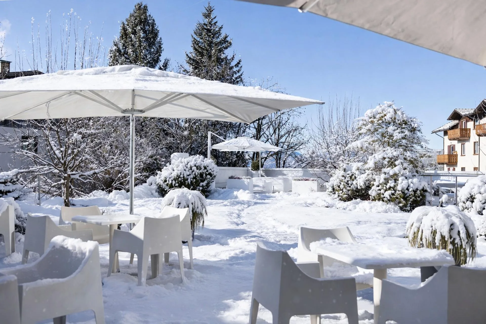 Terrazza esterna con tavoli e sedie bianche, ombrelloni e vegetazione innevata