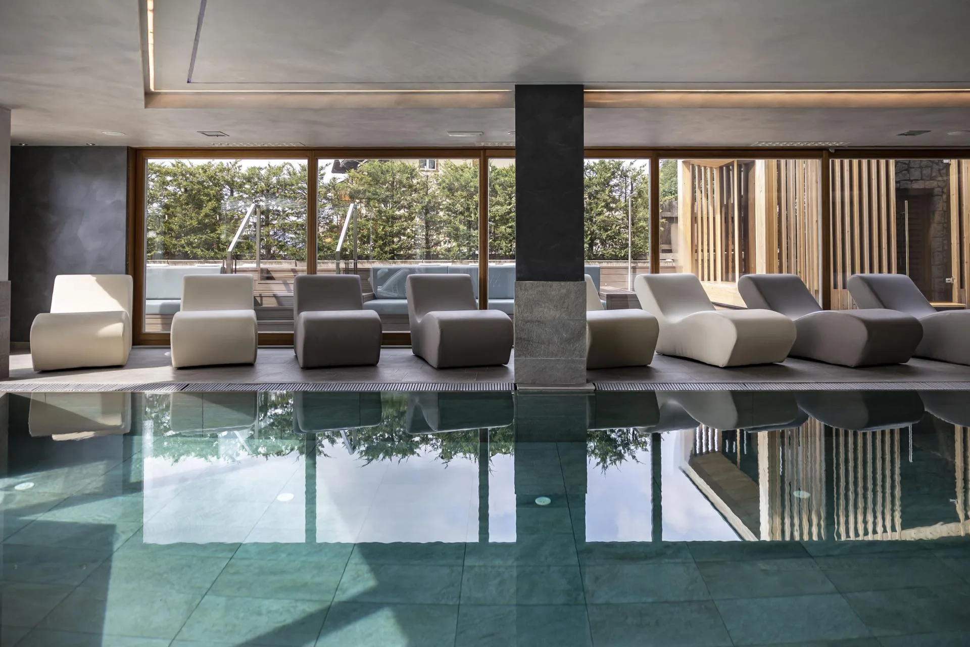 Zona relax della piscina interna con lettini design e vetrate sul verde