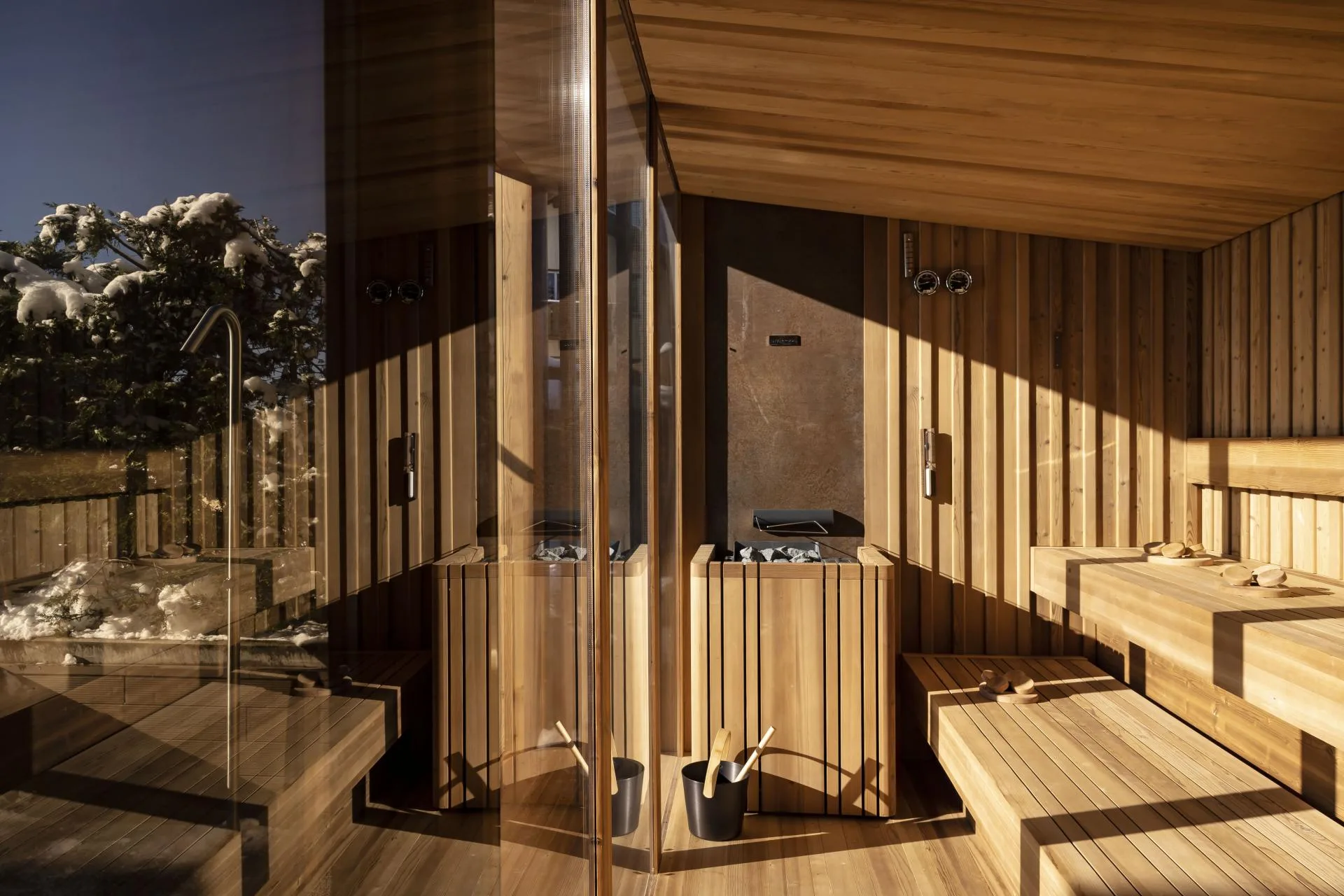 Sauna panoramica in legno con vetrate e vista sulla neve al crepuscolo