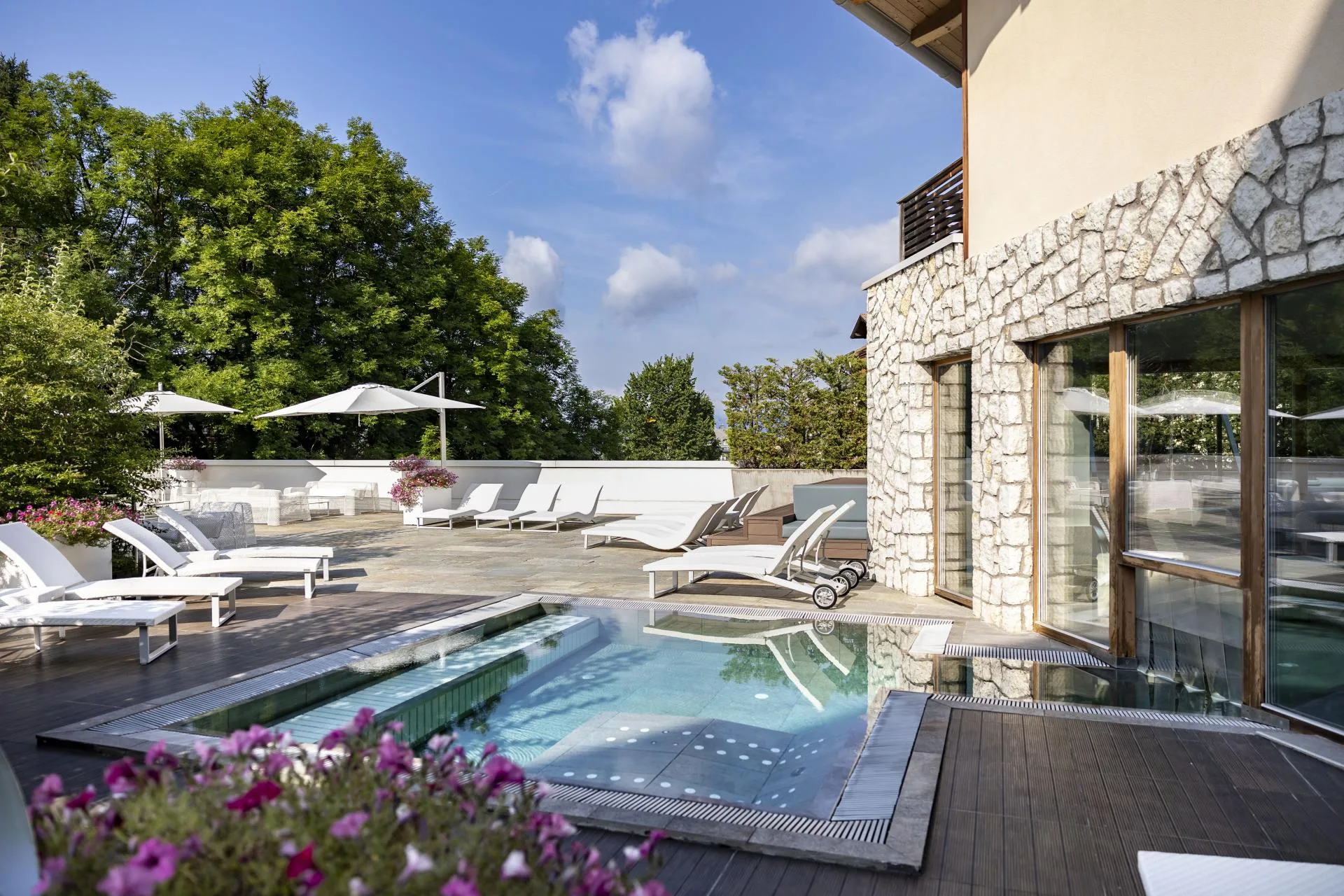 Terrazza estiva con piscina esterna, lettini bianchi, ombrelloni e fiori
