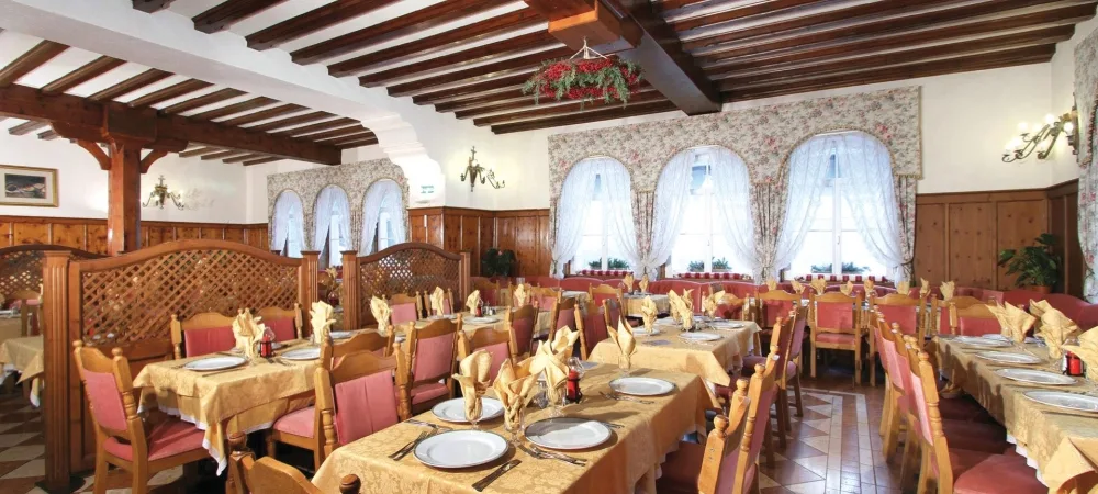 Sala ristorante con soffitto a travi in legno, tavoli apparecchiati e tende fiorate