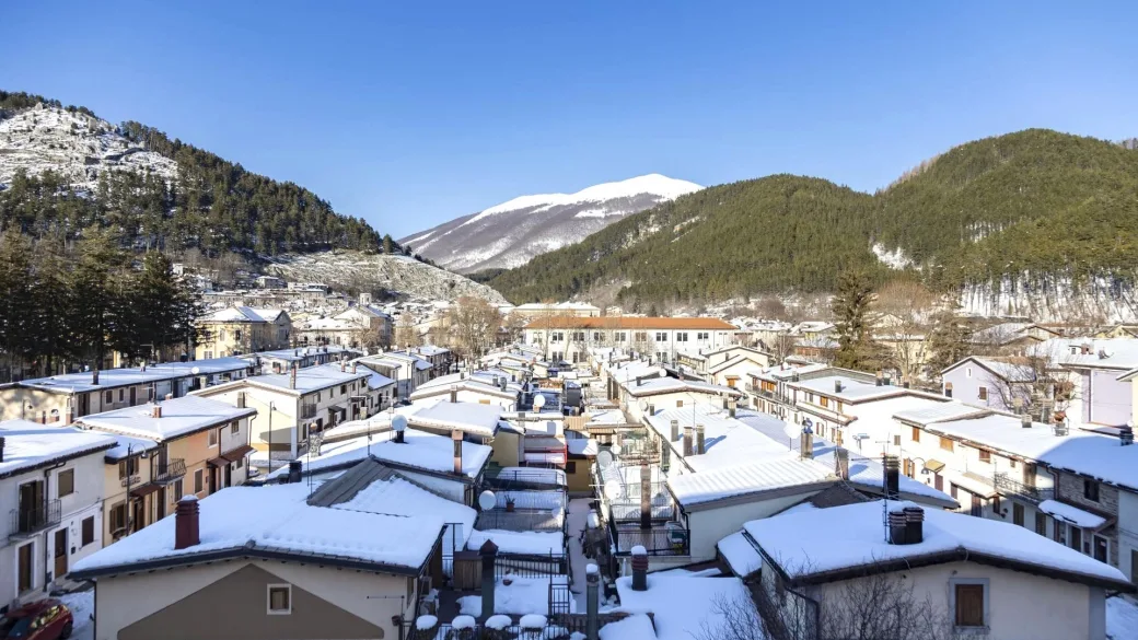 Veduta dall'alto dei tetti innevati del paese con montagne sullo sfondo