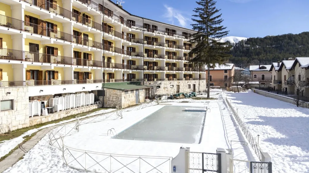 Esterno dell'hotel con piscina innevata, lettini accatastati e abete in giardino