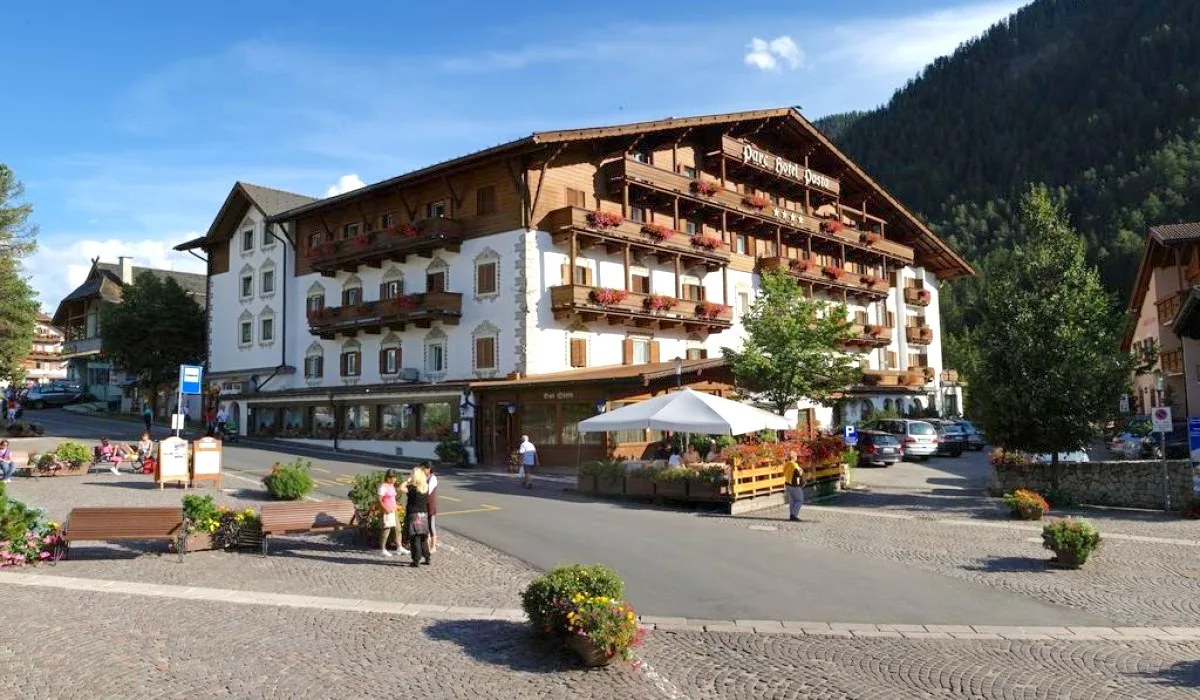 Esterno dell'hotel in estate con terrazza, fiori e montagne sullo sfondo