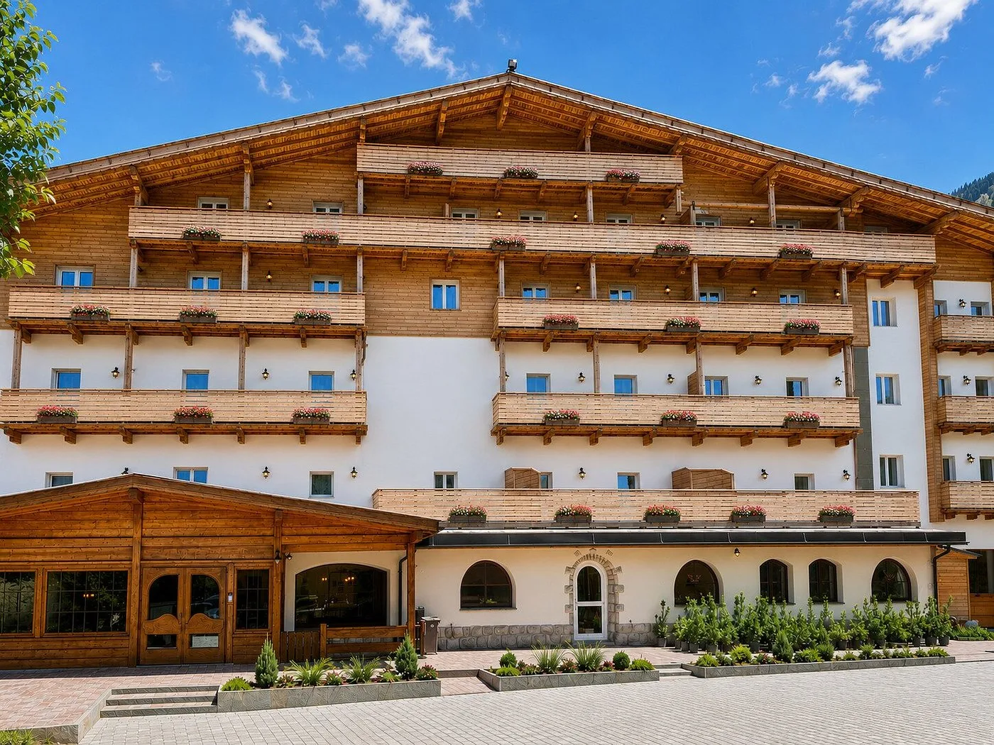 Facciata estiva dell'hotel in stile chalet con balconi fioriti e ingresso in legno